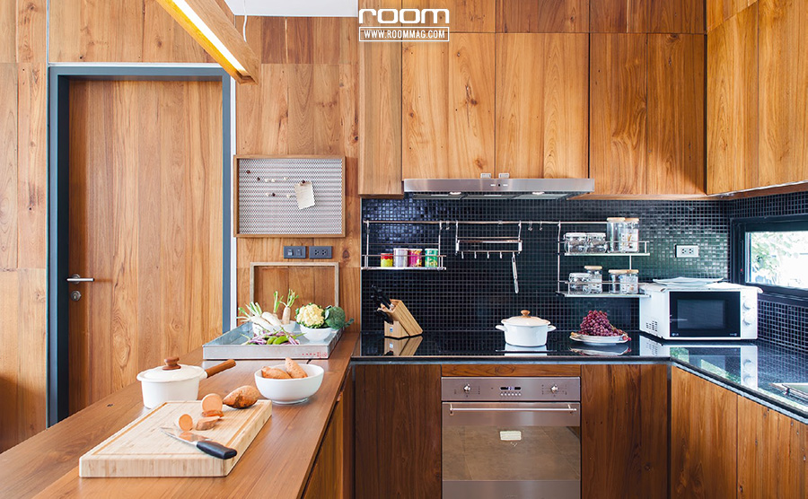 ห้องครัวเชื่อมต่อกับส่วนอื่นของบ้านได้อย่างไม่เคอะเขินด้วยตู้บิลท์อินไม้สัก พื้นที่ประกอบอาหารกรุผนังด้วยกระเบื้องโมเสกสีดํามันเงาให้ผิวสัมผัสที่ดูโมเดิร์น โดดเด่นและแตกต่าง